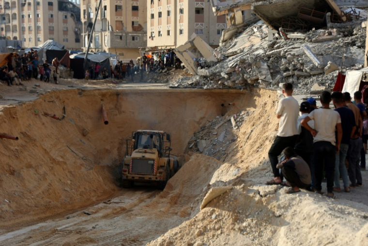 Des Palestiniens regardent une pelleteuse creuser dans le sol à la recherche apparemment de corps à Khan Younès, dans le sud de la bande de Gaza, le 17 octobre 2025 ( AFP / Omar AL-QATTAA )