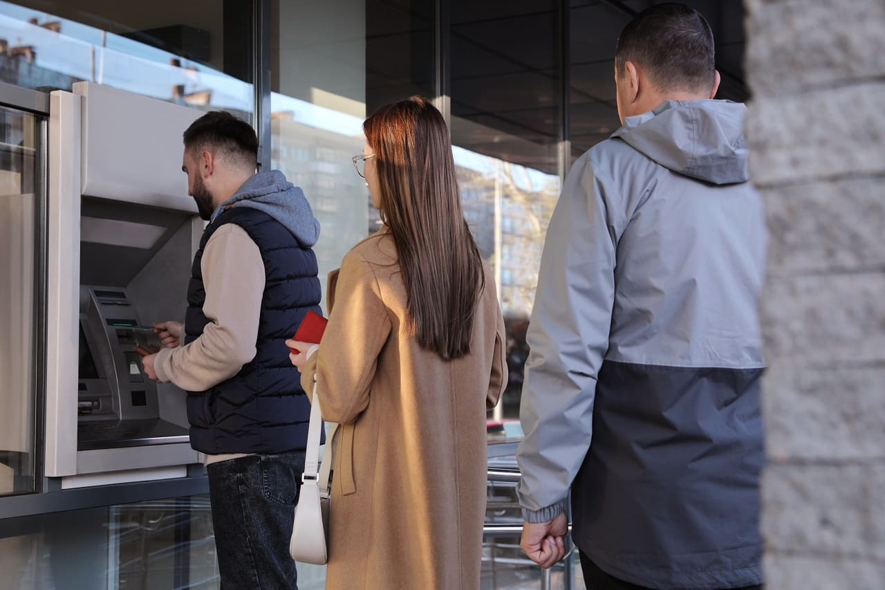 (Crédits photo : Adobe Stock - clients attendant devant un distributeur de billets)