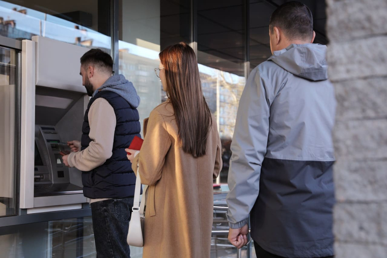 (Crédits photo : Adobe Stock - clients attendant devant un distributeur de billets)