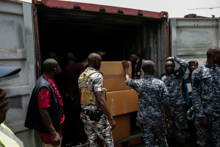 Des membres de l'unité de lutte contre la criminalité organisée transnationale ouvrentl’un des conteneurs saisis contenant des comprimés et gélules de tapentadol en provenance d’Inde, au terminal de Freetown, le 27 mars 2026 en Sierra Leone ( AFP / Saidu BAH )