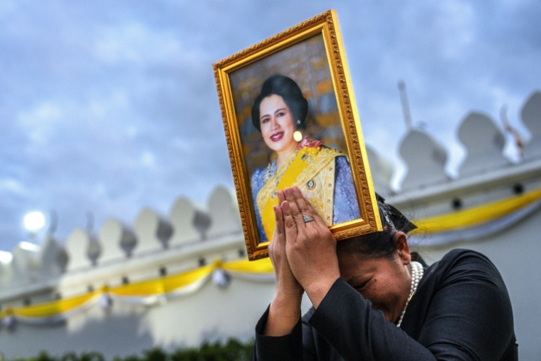 Une femme endeuillée tient un portrait de la reine mère Sirikit de Thaïlande au passage du cortège funéraire, le 26 octobre 2025 à Bangkok ( AFP / Chanakarn Laosarakham )