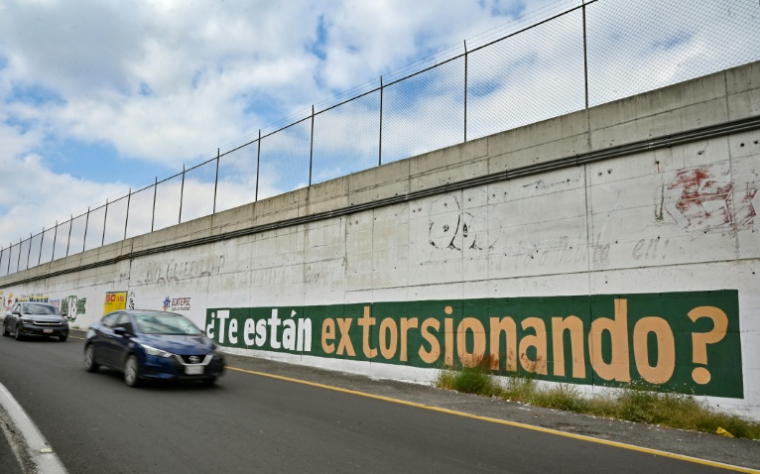 Des automobilistes passent devant un message du gouvernement peint sur un mur exhortant les habitants à signaler les cas d'extorsion à Ecatepec, dans l'Etat de Mexico, le 2 octobre 2025 ( AFP / Yuri CORTEZ )