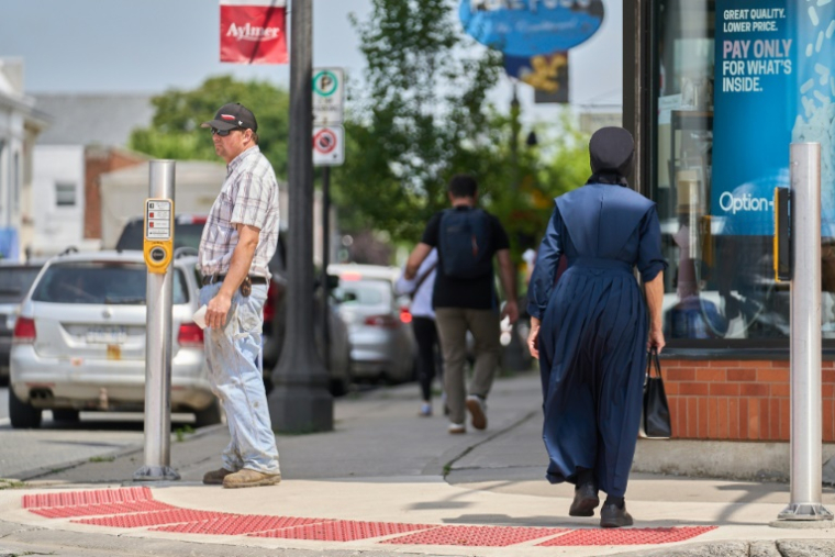Une femme en tenue traditionnelle mennonite dans une rue du centre-ville d'Aylmer, le 9 juillet 2025 au Canada ( AFP / Geoff Robins )