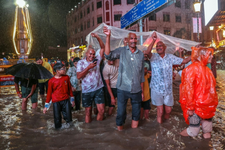 Des habitants s'abritent d'une bâche en plastique dans une rue inondée pendant de fortes pluies de mousson, le 3 octobre 2025 à Varanasi, en Inde ( AFP / Niharika KULKARNI )