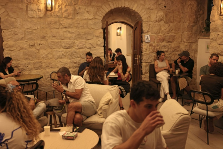 Des Israéliens attablés dans le café Basimta, alors que manifestants ultra-orthodoxes protestent contre l'ouverture durant le shabbat, jour de repos hebdomadaire juif et que des militants laïques organisent une contre-manifestation à Jérusalem, le 15 août 2026. ( AFP / AHMAD GHARABLI )
