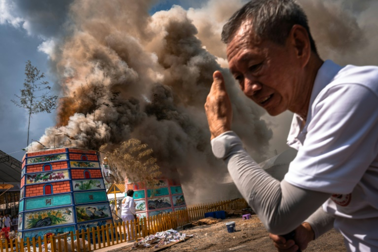 Un volontaire se protége de la chaleur alors que la fumée s'élève des crémations lors de la cérémonie Lang Pacha au complexe de la fondation Dhamma du Bouddha de la région de Nakhon Ratchasima, en Thaïlande, le 23 avril 2025 ( AFP / Chanakarn Laosarakham )