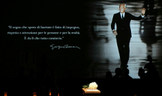 Une photo du défunt créateur de mode Giorgi Armani projetée sur un écran à l'Armani Teatro de Milan où des personnes font la queue pour se recueillir devant son cercueil, le 6 septembre 2025 ( AFP / Stefano RELLANDINI )