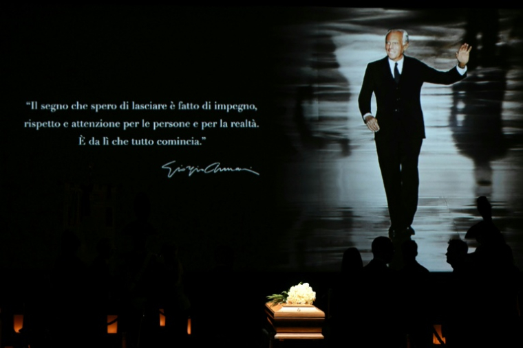 Une photo du défunt créateur de mode Giorgi Armani projetée sur un écran à l'Armani Teatro de Milan où des personnes font la queue pour se recueillir devant son cercueil, le 6 septembre 2025 ( AFP / Stefano RELLANDINI )