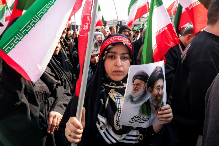 Une Iranienne tient une photo du nouveau guide suprême iranien, l'ayatollah Mojtaba Khamenei (d), et de son défunt père, Ali Khamenei, lors d'un rassemblement de soutien à Téhéran, le 9 mars 2026 ( AFP / ATTA KENARE )