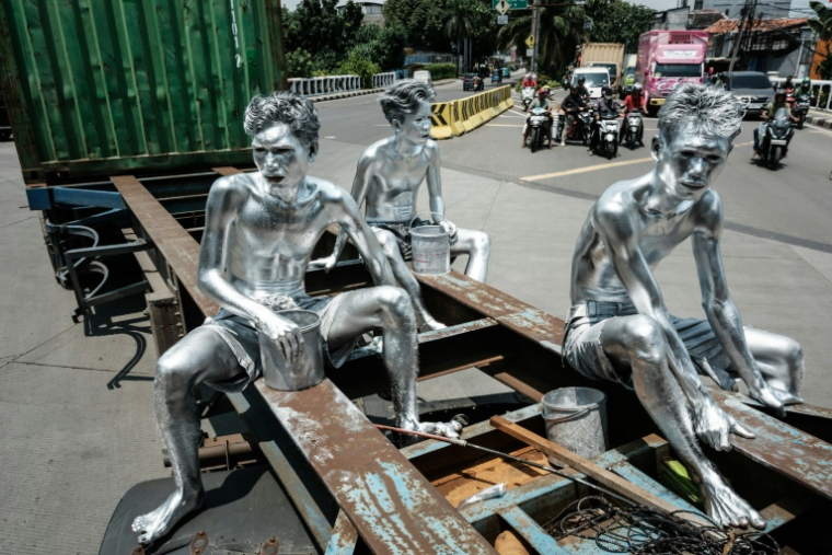 Les artistes de rue Keris Munandar (d), son frère Ari Munandar (g) et leur voisin Riyan Ahmad Fazriyansah assis sur la remorque d'un camion porte-conteneurs à Jakarta, le 7 avril 2025 en Indonésie ( AFP / Yasuyoshi CHIBA )