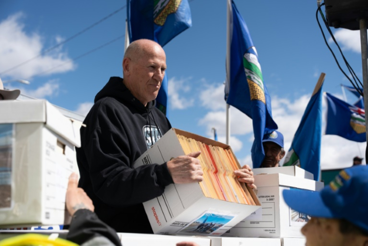 Le chef de file des séparatistes de l'Alberta Mitch Sylvestre, tenant un carton contenant des petitions demandant la tenue d'un vote, le 4 mai 2026 devant les locaux d'Elections Canada, à Edmonton (Canada). ( AFP / Henry MARKEN )