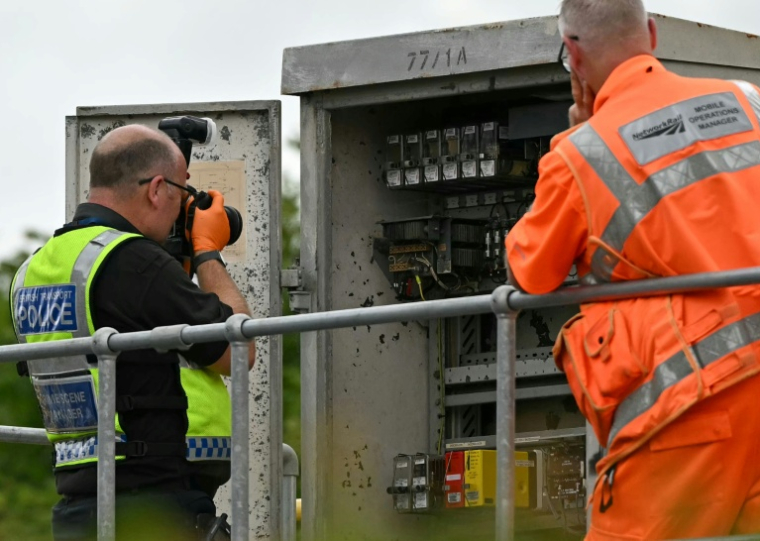 Un membre de la police des transports britannique photographie l'intérieur d'un boîtier de localisation (LOC) en bordure de voie, près du site d'une collision entre deux trains de l'East Midlands Railway (EMR) survenue la veille, le 20 juin 2026 au sud de Bedford, dans le centre de l'Angleterre ( AFP / JUSTIN TALLIS )