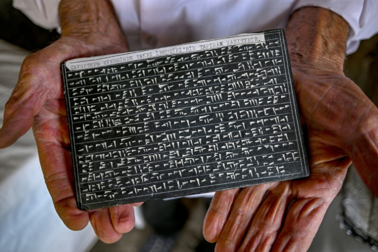 Mehmet Kusman tient une tablette sur laquelle il a gravé des inscriptions en urartéen à la forteresse de Cavustepe, près de Van, dans l'est de la Turquie, le 22 juillet 2026 ( AFP / Ozan KOSE )