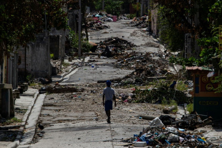 Une personne marche le 25 septembre 2025 parmi les décombres dans une rue du quartier de Delmas 30 à Port-au-Prince, en Haïti, quartier ayant subi plusieurs attaques de gangs ( AFP / Clarens SIFFROY )