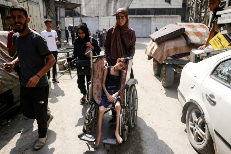 Une Palestinienne pousse le fauteuil roulant d'un enfant fuyant avec d'autres le quartier d'Abu Iskandar, au nord de la ville de Gaza, le 22 août 2025 ( AFP / Bashar TALEB )