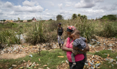 Hélène Mvubu porte sa fille en marchant dans un champ pollué à Lubumbashi en République démocratique du Congo le 24 novembre 2025 ( AFP / Glody MURHABAZI )