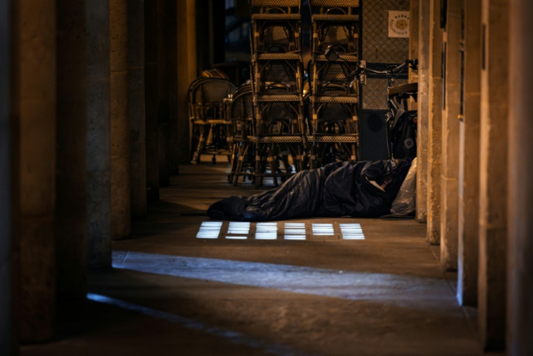 Un homme dort dans un sac de couchage à proximité d'une terrasse de café le 15 octobre 2025 à Paris  ( AFP / JOEL SAGET )