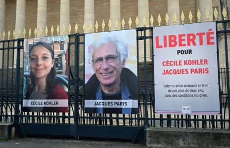 Les portraits de Cécile Kohler et de Jacques Paris, emprisonnés en Iran, accrochés aux grilles de l'Assemblée nationale à Paris, le 25 mars 2025 ( AFP / Bertrand GUAY )