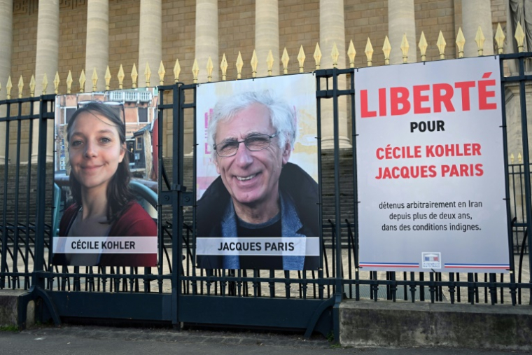 Les portraits de Cécile Kohler et de Jacques Paris, emprisonnés en Iran, accrochés aux grilles de l'Assemblée nationale à Paris, le 25 mars 2025 ( AFP / Bertrand GUAY )