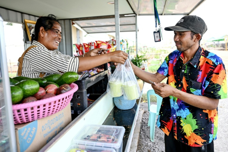 Im Chreb (g), propriétaire d'un café, vend des smoothies à un client dans un "village d'attente" du district de Svay Chek, dans la province de Banteay Meanchey, le 24 août 2026au Cambodge ( AFP / TANG CHHIN Sothy )