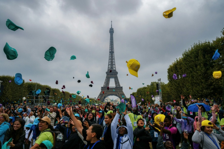 Des enfants jettent leur casquette alors qu'ils assistent à un concert au Champ-de-Mars avec la Tour Eiffel en arrière-plan à Paris, dans le cadre de la 46e édition d'une journée d'activités pour les enfants qui ne partent pas en vacances, organisée par le Secours Populaire ( AFP / Dimitar DILKOFF )