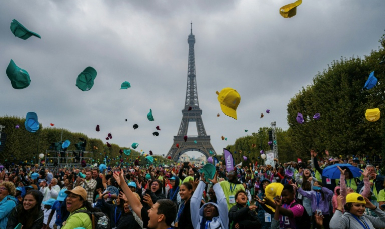 Des enfants jettent leur casquette alors qu'ils assistent à un concert au Champ-de-Mars avec la Tour Eiffel en arrière-plan à Paris, dans le cadre de la 46e édition d'une journée d'activités pour les enfants qui ne partent pas en vacances, organisée par le Secours Populaire ( AFP / Dimitar DILKOFF )