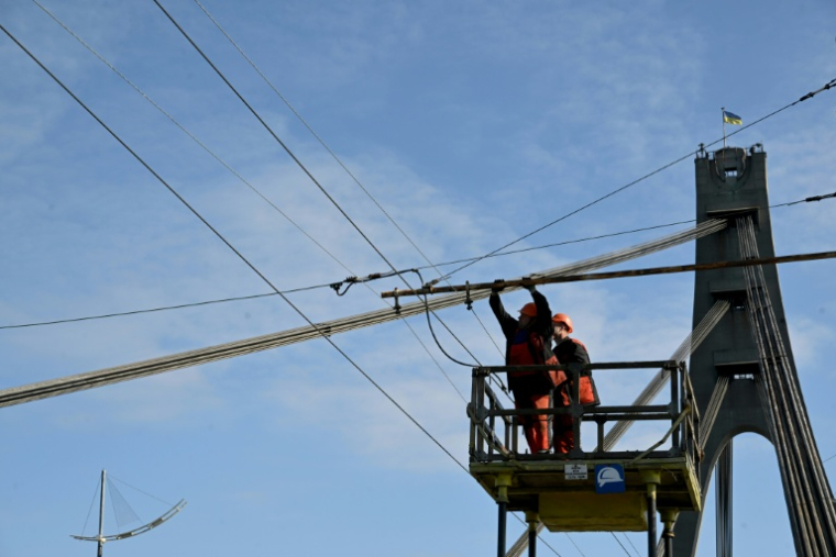Des techniciens réparent une ligne électrique de trolleybus endommagée à la suite d'une attaque de drone contre le pont du Nord à Kiev, le 3 octobre 2026 ( AFP / Sergei SUPINSKY )