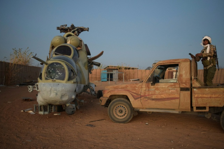 Un combattant du Front de libération de l'Azawad (FLA), rébellion à dominante touareg, se tient sur un pick-up à côté d'une carcasse d'hélicoptère russe Mi-24 dans l'ancien camp du groupe paramilitaire russe Africa Corps à Kidal (Mali), le 6 mai 2026 ( AFP / - )