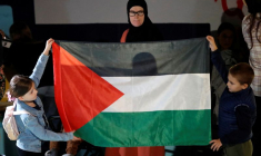 Une femme regarde des enfants tenant un drapeau palestinien