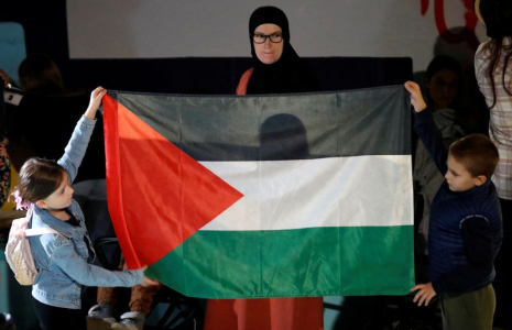 Une femme regarde des enfants tenant un drapeau palestinien