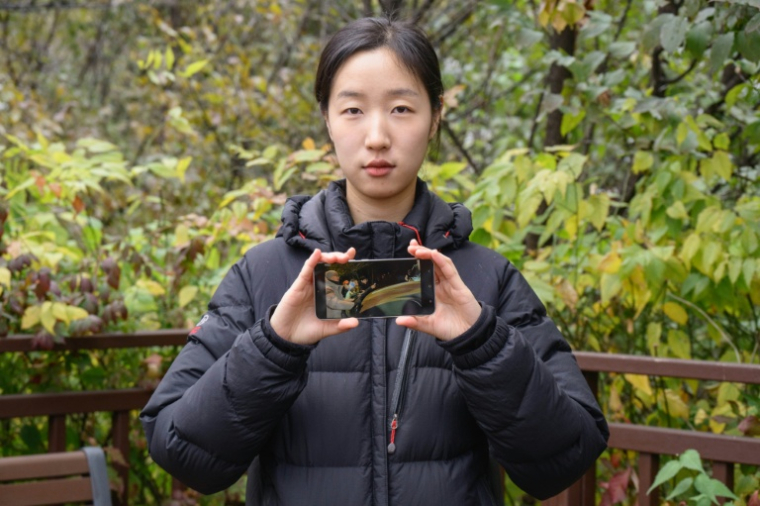 L'étudiante sud-coréenne Kim Da-in montre une photo, prise par sa mère, d'elle en train de barrer la route à un véhicule militaire se dirigeant vers l'Assemblée nationale pendant la loi martiale, le 23 novembre 2025 à Séoul ( AFP / Anthony WALLACE )