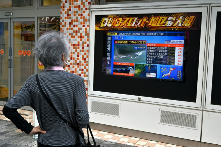 Une passante regarde un écran de télévision diffusant une alerte au tsunami à Tokyo, le 30 juillet 2025 ( AFP / Richard BROOKS )