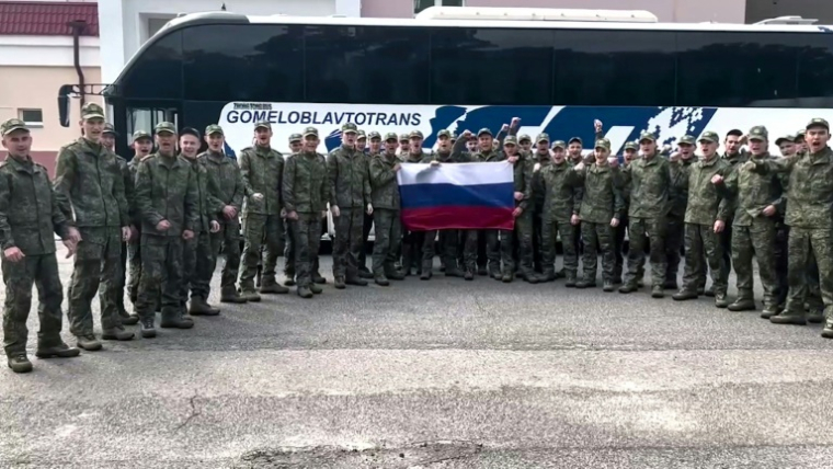 Image tirée d'une vidéo diffusée par le ministère russe de la Défense, le 9 juin 2025, de prisonniers de guerre russes tenant un drapeau russe devant un bus après un échange dans un lieu non divulgué au Bélarus ( Ministère russe de la Défense / Handout )