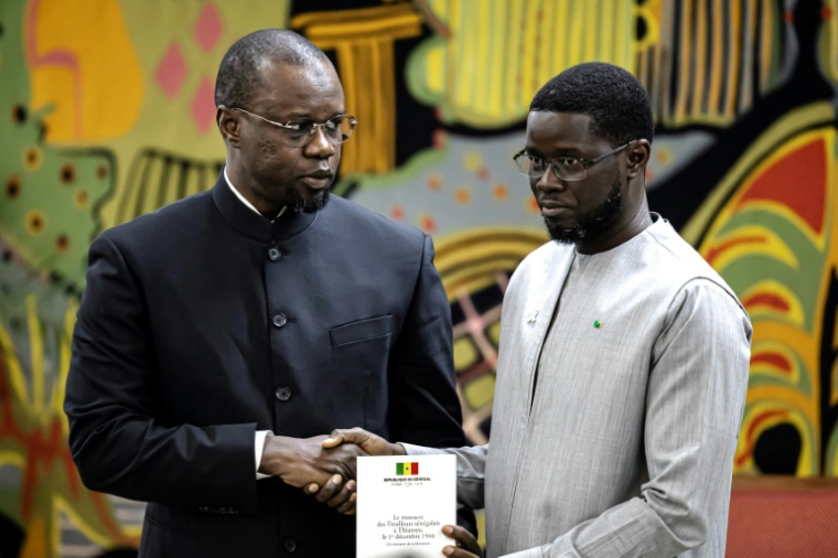 Le Premier ministre Ousmane Sonko (g) remet au président Bassirou Diomaye Faye (d) un Libre blanc sur le massacre de tirailleurs africains par l'armée coloniale française en 1944, le 16 octobre 2025 à Dakar, au Sénégal ( AFP / PATRICK MEINHARDT )