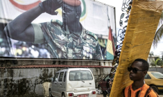 Un vendeur ambulant dans la capitale guinéenne Conakry passe le 11 septembre 2021 devant une pancarte à l'effigie du chef de la junte Mamadi Doumbouya. Le général est officiellement entré le 3 novembre 2025 dans la course à la présidentielle du 28 décembre prochain après avoir déposé son dossier de candidature à ce scrutin ( AFP / JOHN WESSELS )