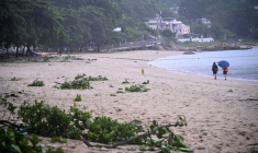 Des personnes se promènent sur une plage jonchée de débris laissés par le typhon Noul, à Hong Kong, le 26 juillet 2026 ( AFP / Peter PARKS )