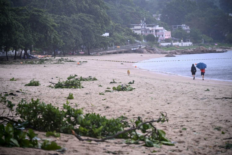 Des personnes se promènent sur une plage jonchée de débris laissés par le typhon Noul, à Hong Kong, le 26 juillet 2026 ( AFP / Peter PARKS )