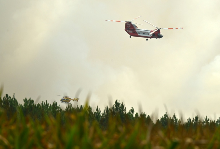 Un hélicoptère bombardier d'eau CH-47D Chinook du Rural Fire Service (RFS) de Nouvelle-Galles du Sud (Australie) et un hélicoptère de la Sécurité civile française survolent la forêt de Luglon lors d'un incendie de forêt, le 14 août 2026 dans les Landes ( AFP / Gaizka IROZ )