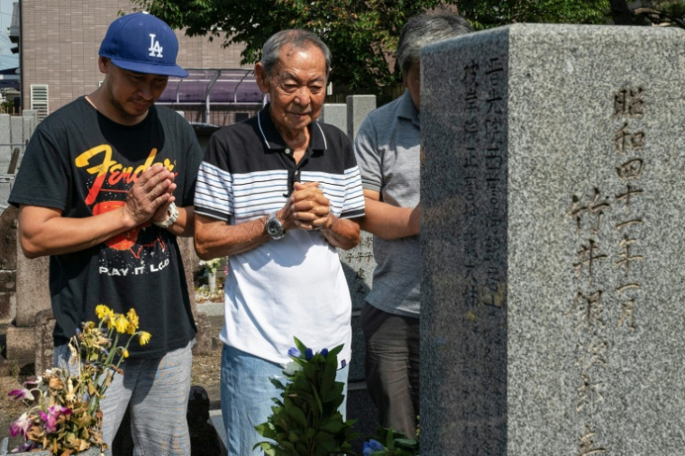 Jose Villafuerte (au centre) prie avec son fils sur la tombe de son père à Takatsuki, au Japon, le 7 août 2025 ( AFP / Fred MERY )