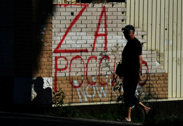 Un homme devant une inscription "Pour la Russie", dans la cité portuaire ukrainienne de Marioupol, contrôlée par la Russie, le 15 juillet 2025 ( AFP / Olga MALTSEVA )