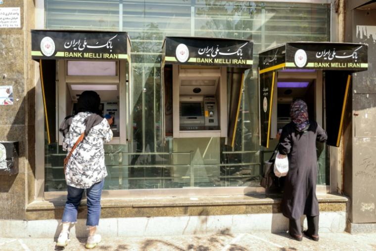 Des passantes retirent de l'argent à un distributeur de billets dans une rue de Téhéran, le 28 septembre 2025 en Iran ( AFP / ATTA KENARE )