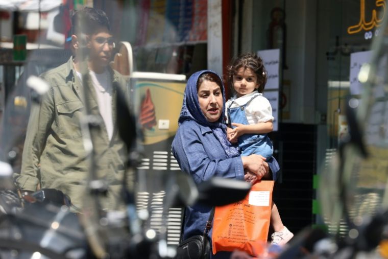 Une femme porte une enfant dans ses bras dans une rue de Téhéran, le 27 avril 2026 en Iran ( AFP / ATTA KENARE )