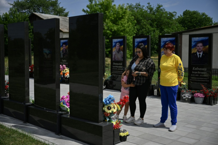 Nadia (à droite), 57 ans, mère du soldat ukrainien Andriï Doubnytsky, aujourd'hui décédé, sa veuve Lioudmyla (au centre), 27 ans, et leur fille Mia (à gauche), 4 ans, posent devant son portrait lors de leur visite au cimetière du village de Stepantsi, dans la région de Tcherkassy, le 7 juillet 2026. ( AFP / Genya SAVILOV )
