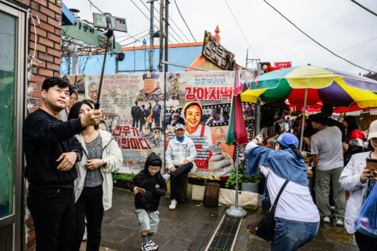 Sur cette photo prise le 7 octobre 2025, des visiteurs prennent des photos et des selfies dans un marché de l'île de Gyodong ( AFP / ANTHONY WALLACE )