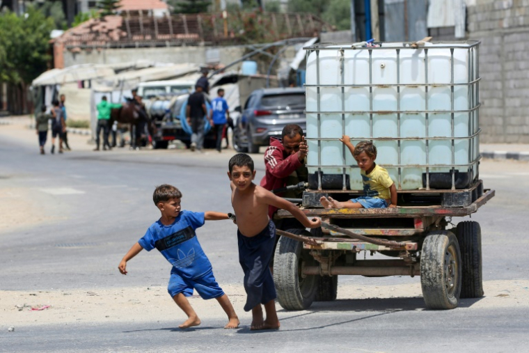 Un homme et des enfants poussent un chariot transportant un réservoir d'eau à Bureij dans le centre de la bande de Gaza, le 17 août 2025 ( AFP / Eyad BABA )