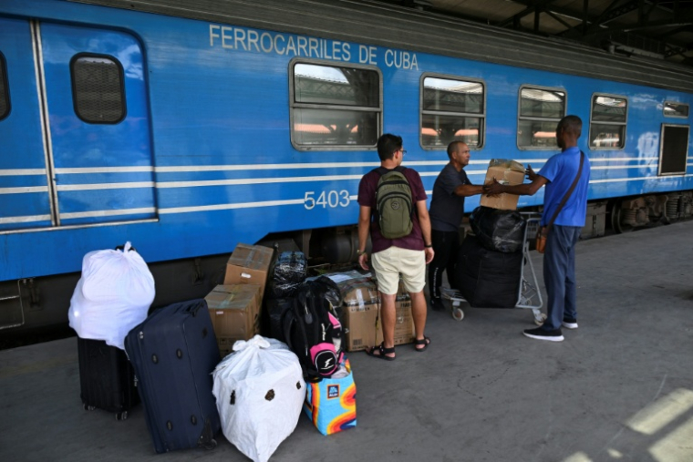 Des hommes se tiennent près de bagages et de cartons empilés sur un quai, devant un train de Ferrocarriles de Cuba, à La Havane, le 16 juin 2026 ( AFP / YAMIL LAGE )