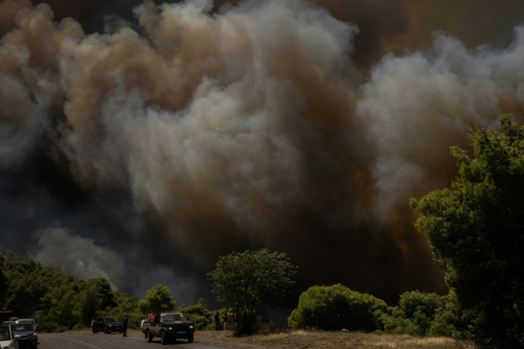 Des véhicules de secours stationnés au premier plan tandis que de la fumée s’élève d’un incendie de forêt à l’arrière-plan, dans la région de Porto Germeno, le 1er août 2026 ( AFP / Angelos TZORTZINIS )