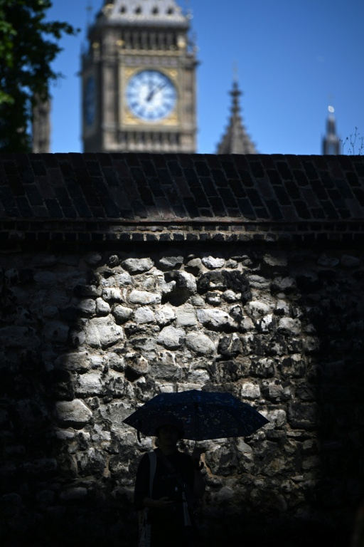 Un passant se protège de la chaleur sous un parapluie près des Chambres du Parlement à Londres, le 12 juillet 2025 ( AFP / Justin TALLIS )