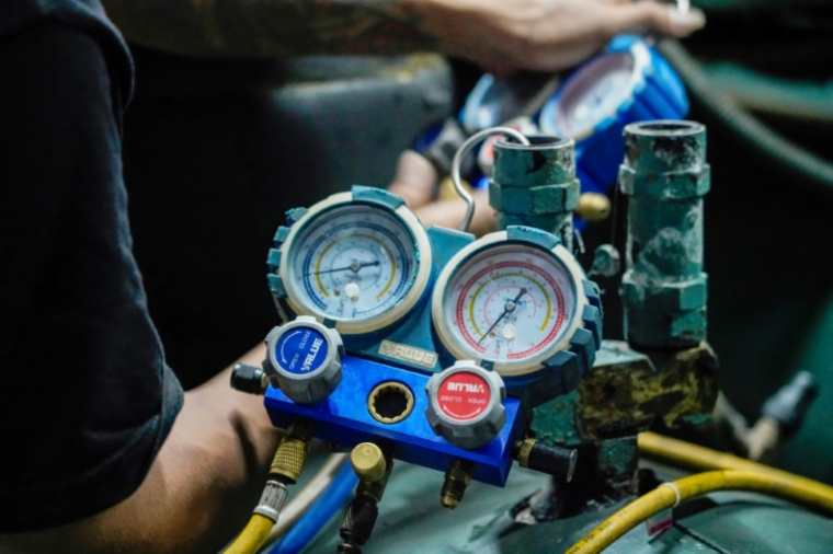 Des techniciens de la société Recoolit suivent sur des jauges le captage des gaz de refroidissemen d'une grande unité de climatisation au sous-sol d'un complexe d'habitation à Jakarta, le 10 juin 2025 en Indonésie ( AFP / Jack Moore )
