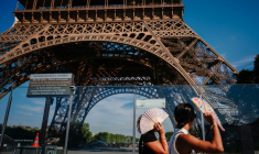 Des touristes se protègent du soleil avec des éventails en passant devant la tour Eiffel, fermée plus tôt en raison de la canicule, le 11 juillet 2026 à Paris ( AFP / Dimitar DILKOFF )